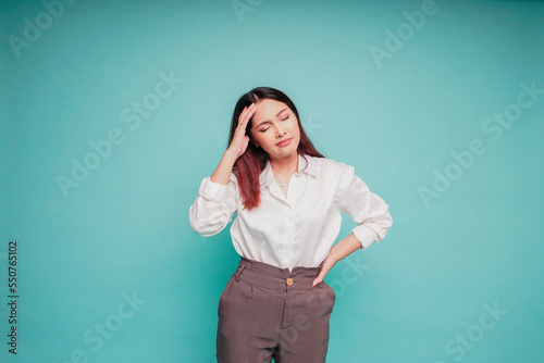 A portrait of an Asian woman wearing a white shirt isolated by blue background looks depressed