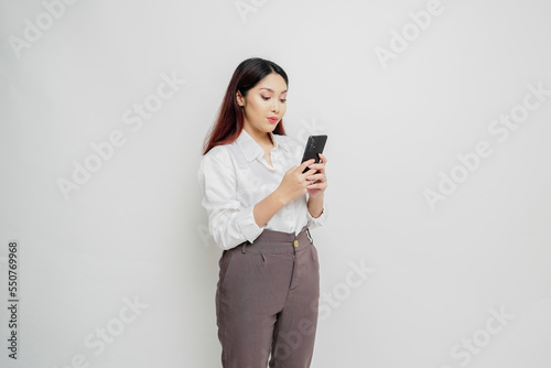 A portrait of a happy Asian woman wearing a white shirt and holding her phone, isolated by white background