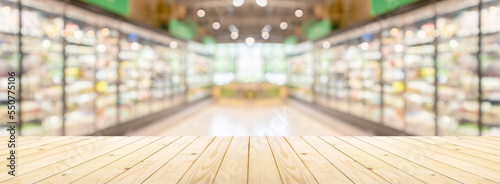Empty wood table top with supermarket grocery store aisle and shelves blurred background © Kwangmoozaa