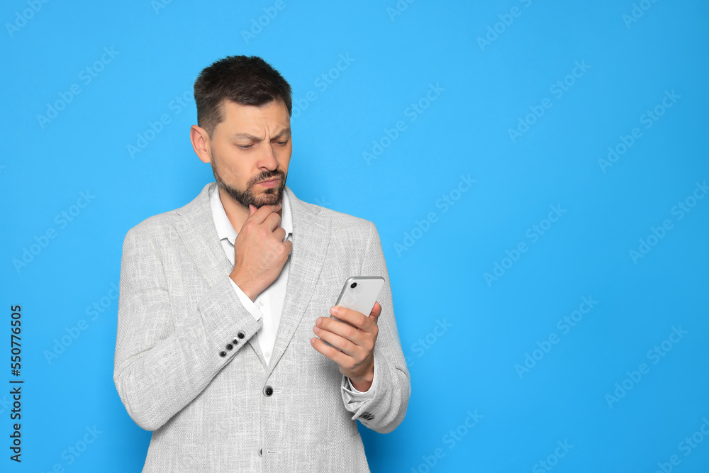 Pensive man looking at smartphone on light blue background. Space for text Pensive man looking at smartphone on light blue background. Space for text