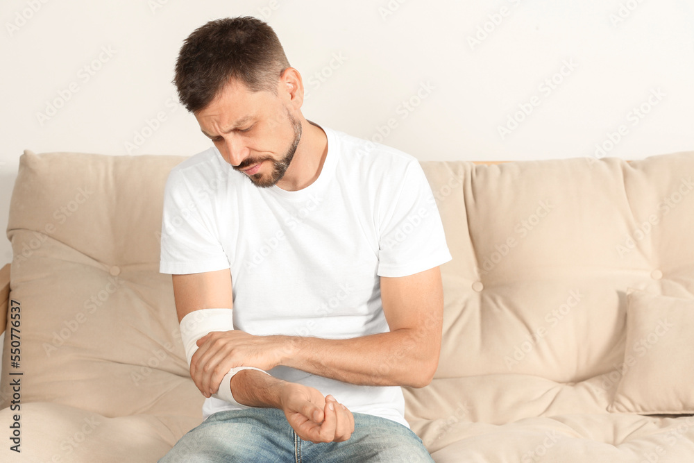 Man with arm wrapped in medical bandage on sofa indoors
