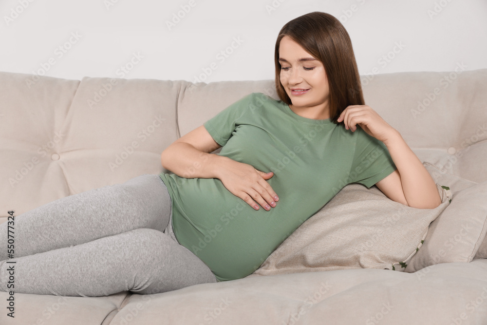 Happy pregnant woman lying on beige sofa indoors Happy pregnant woman lying on beige sofa indoors
