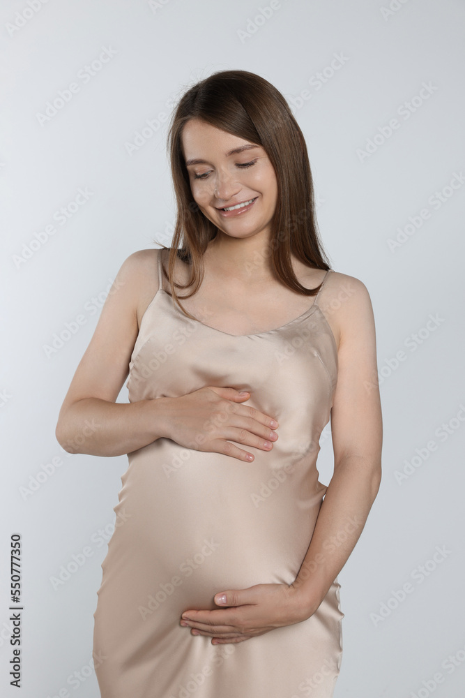 Happy pregnant woman touching belly on light grey background Happy pregnant woman touching belly on light grey background