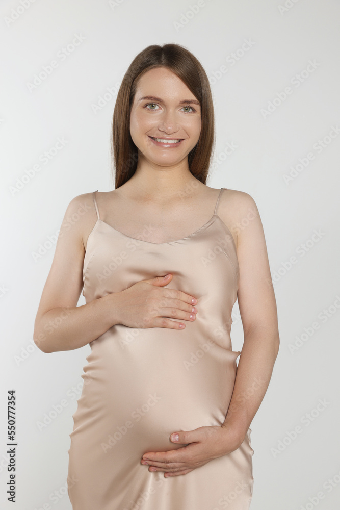 Happy pregnant woman touching belly on light grey background Happy pregnant woman touching belly on light grey background
