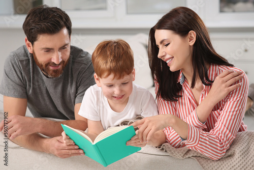 Happy parents with their child reading book on couch at home