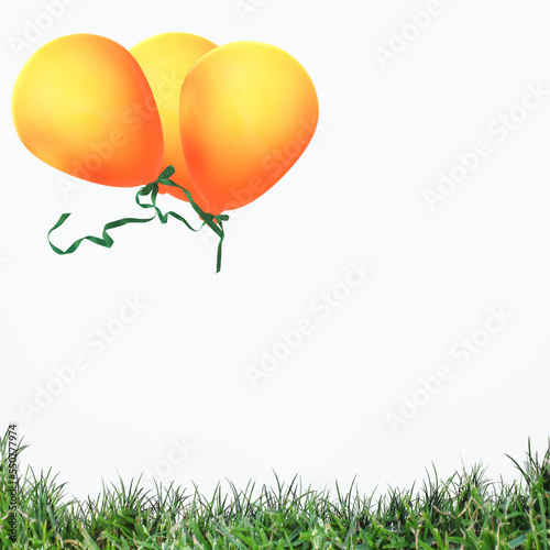 zwei orange Luftballons mit grünen Bändern schweben über Gras