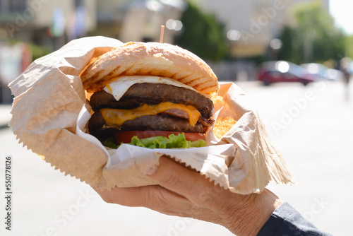 Woman holding delicious burger in paper wrap on city street, closeup