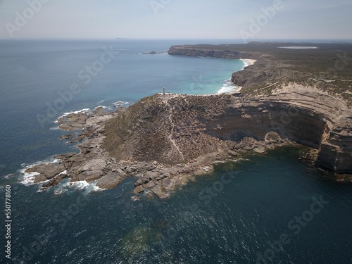 Aerial view of the sea waves splashing over cliffs on the shore with a blue sky in the background photo