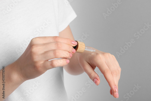 Woman dripping serum from pipette on her hand against light grey background, closeup