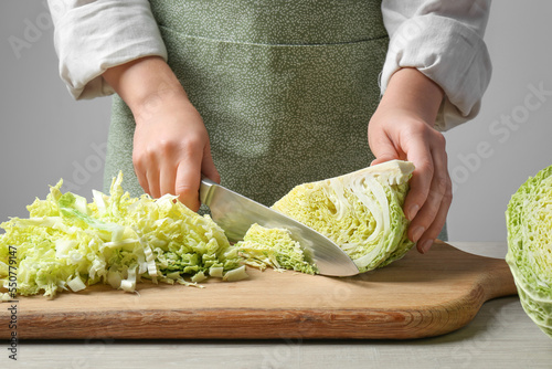 Woman cutting fresh savoy cabbage on board at wooden table, closeup
