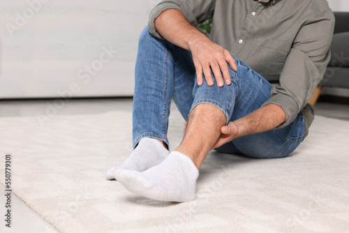 Man suffering from leg pain on white carpet indoors, closeup