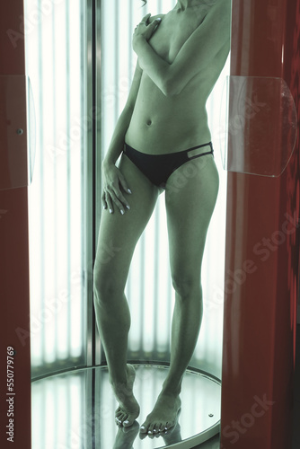 Cropped image slender topless pretty woman enjoying tanning in modern vertical solarium in SPA salon. Slim lady in solarium, gets pleasure and enjoy. Concept of healthy lifestyle. Copy text space