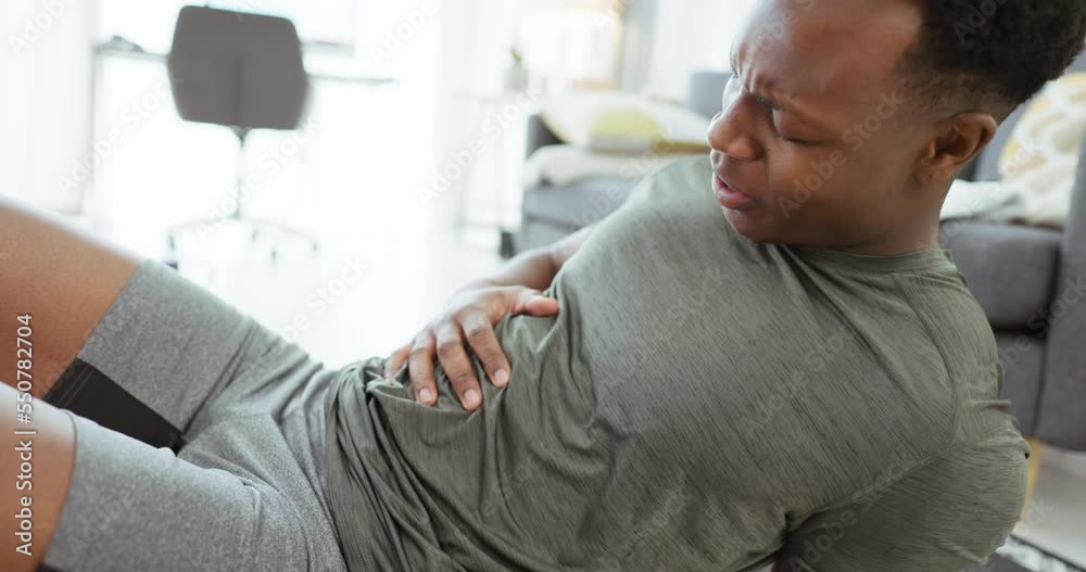 Exercise, pain and black man with an injury after workout, fitness and training in home living room. Healthcare, accident and person feeling his body with appendicitis and medical emergency in home Exercise, pain and black man with an injury after workout, fitness and training in home living room. Healthcare, accident and person feeling his body with appendicitis and medical emergency in home