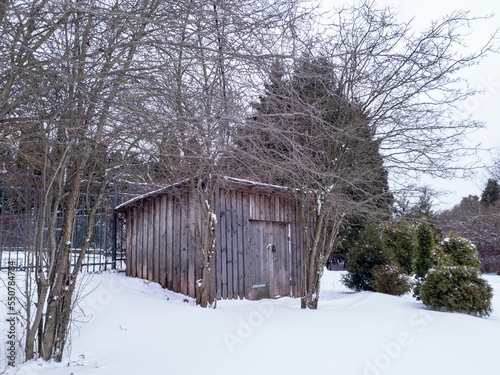 A simple wooden shed in a snowy forest in winter. A utility building in a park or botanical garden.