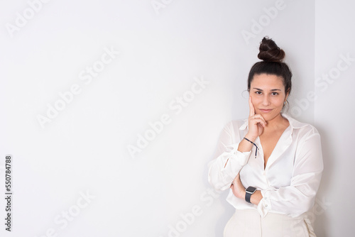 portrait on white wall of an empowered young woman in white executive clothes