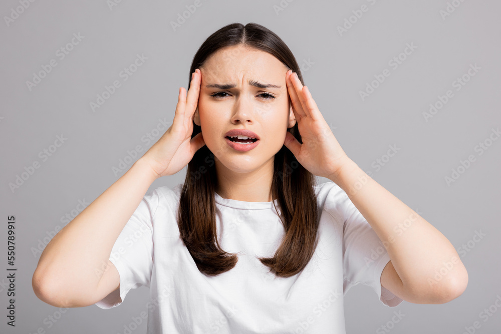 Young beautiful brunette woman wearing white t-shirt over grey isolated background suffering from headache desperate and stressed because pain and migraine. Hands on head. Young beautiful brunette woman wearing white t-shirt over grey isolated background suffering from headache desperate and stressed because pain and migraine. Hands on head.