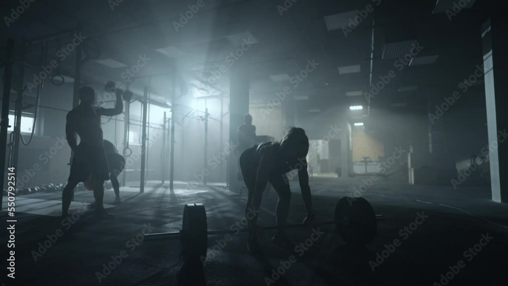 four sportspersons are training hard in gym, woman is lifting barbell, silhouette in darkness four sportspersons are training hard in gym, woman is lifting barbell, silhouette in darkness