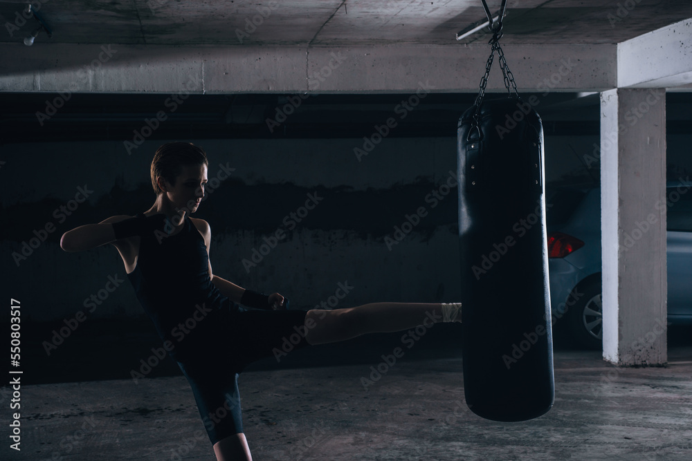 Silhouette picture of young female kicking the boxing bag