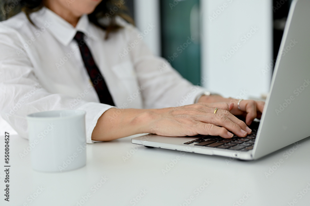 Professional Asian aged businesswoman working at her desk, using laptop, typing on keyboard. Professional Asian aged businesswoman working at her desk, using laptop, typing on keyboard.
