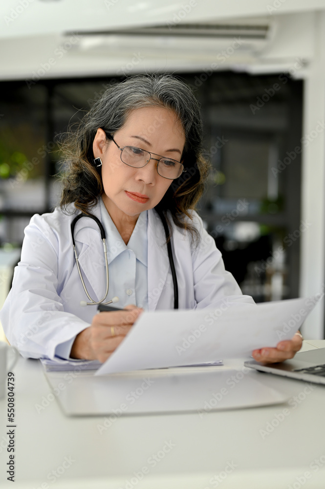 Portrait, Smart Asian aged female doctor focusing on reading a medical research case Portrait, Smart Asian aged female doctor focusing on reading a medical research case