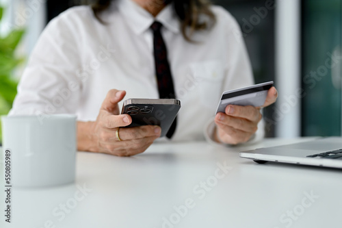 An aged woman holding a credit card and using her smartphone to pay an online bills.
