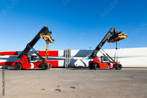 A four-wheeled mobile container loaders parked at the seaport, next to the storage blades for wind turbines.