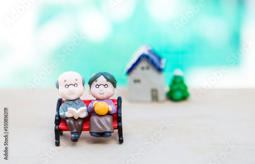 Miniature elderly couple sitting on the bench over blurred house, eldery home care concept