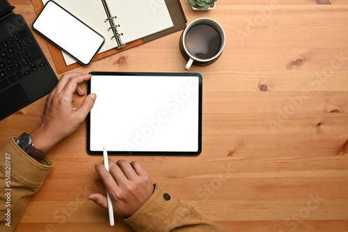 Hipster man hand holding stylus pen and using digital tablet on wooden table. Flat lay, Top view with copy space
