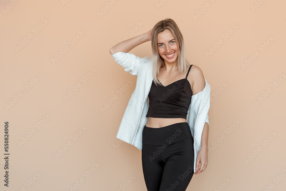 Portrait of lovely young woman with freckles posing in white blazer and black clothes over beige background. Young emotional woman Portrait of lovely young woman with freckles posing in white blazer and black clothes over beige background. Young emotional woman