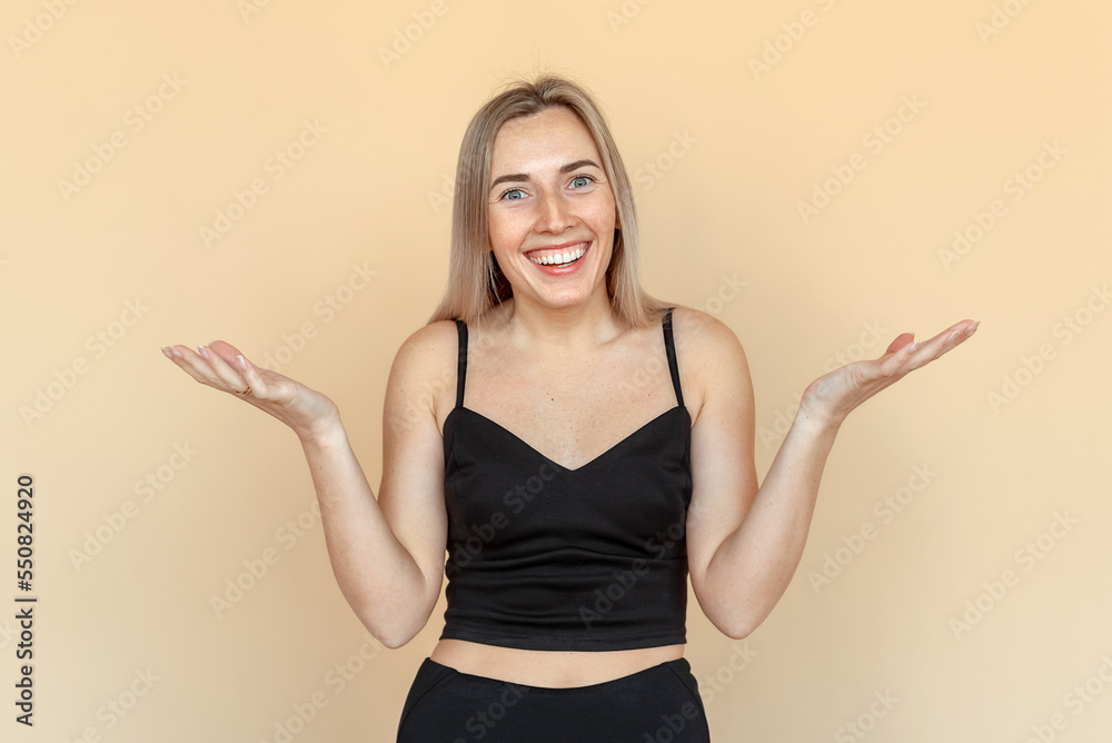 Portrait of happy young woman with freckles posing against beige background. Beautiful female model smiling and gesturing hands