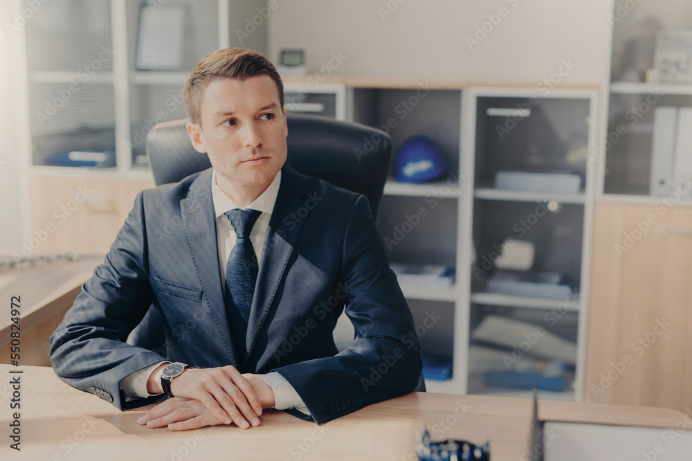 Portrait of thoughtful businessman in elegant suit sits in office at his cabinet, ponders on creating new business plan, ponders about strategies to raise sales, going to have work break in restaurant Portrait of thoughtful businessman in elegant suit sits in office at his cabinet, ponders on creating new business plan, ponders about strategies to raise sales, going to have work break in restaurant