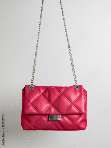 Quilted crossbody bag in red Viva Magenta color with metal chain strap on neutral light background. Demonstrating color of 2023 year in apparel and fashion industry