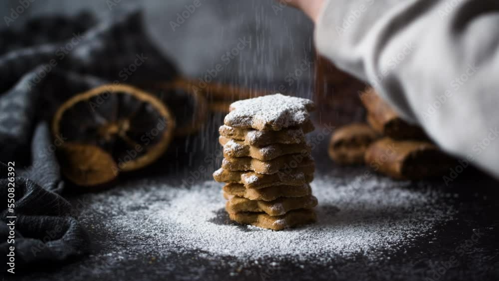 Child hands spreading Sugar Powder On Cookies. Powdered sugar falls on homemade Christmas cookies in shape of stars on rustic Backround surrounded by gingerbread and dried oranges. Decorated.
