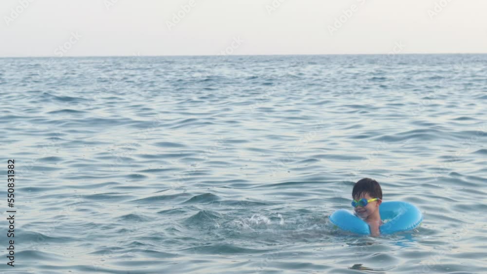 kid swimming in sea water with blue color inflatable ring splashing water with legs smiling having fun family summer vacation.child boy with goggles on eyes rotative moves with ring learn to swim 4k kid swimming in sea water with blue color inflatable ring splashing water with legs smiling having fun family summer vacation.child boy with goggles on eyes rotative moves with ring learn to swim 4k