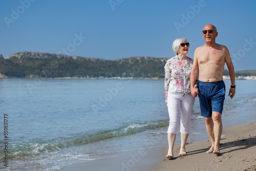coppia di anziani coniugi presi per mano  camminano lungo la battigia di una spiaggia 