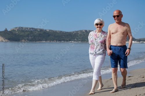 coppia di anziani coniugi presi per mano  camminano lungo la battigia di una spiaggia  photo