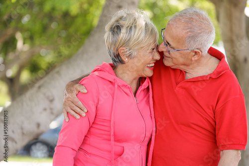 coppia di anziani con abiti sportivi molto sgargianti  si abbraccia felice in un parco photo