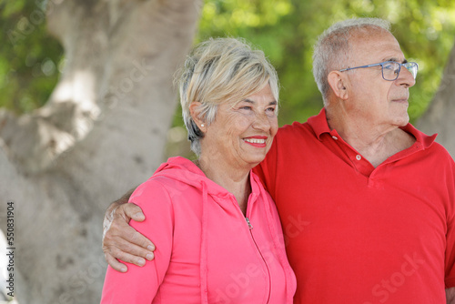 coppia di anziani con abiti sportivi molto sgargianti si abbraccia felice in un parco
