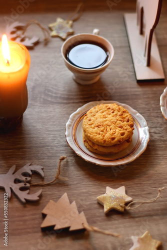 Two types of cookies, cups of tea or coffee, various Christmas decorations and lit candles. Cozy Christmas atmosphere at home. Selective focus.