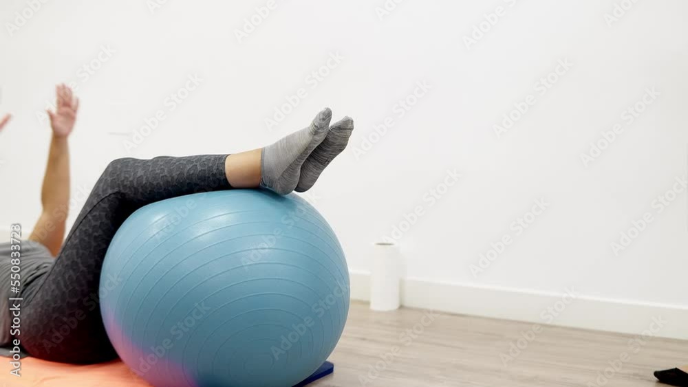 a young Caucasian woman performing a corrective exercise using a physio exercise ball in a sports physiotherapy clinic