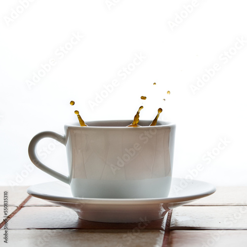 Splashes and splashes over a white cup of coffee standing on a ceramic tiled table