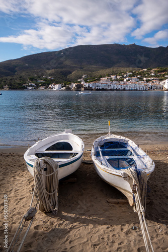 Barcas de jóvenes pescadores estacionadas en la arena de una de las playas del pueblo de cadaqués mirando hacia el tranquilo mar con la verde montaña de fondo.