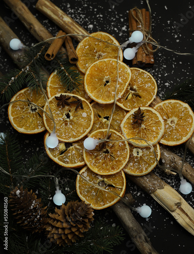 dried oranges cones cinnamon fir branches and star anise beautifully laid out on wooden natural sticks christmas decoration on a dark background with snow and garlands. for cards calendar labels signa