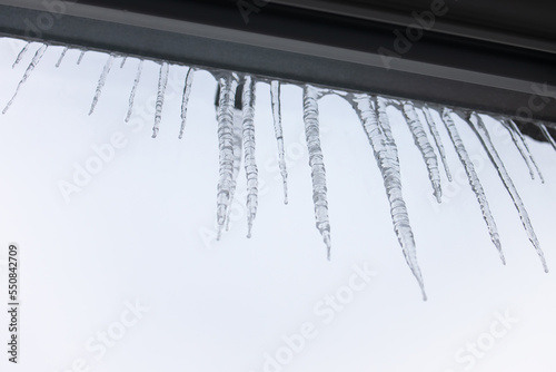 Sharp icicles hanging from eaves of roof. Beautiful transparent icicles slowly gliding of a roof. View from inside