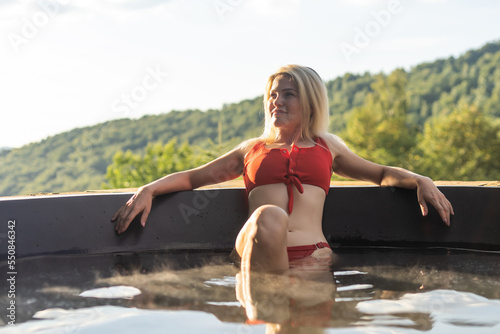 Woman relaxing in hot bath outdoors, enjoying thermal spa at mountains. summer holidays in the mountains, hot water treatments concept.