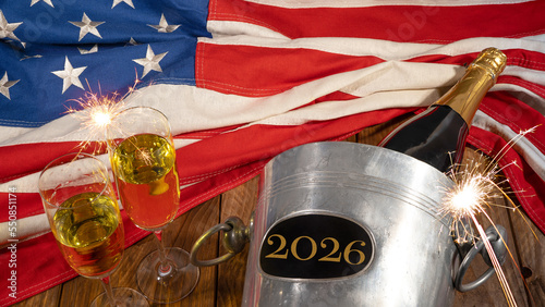 New Year 2026 New Year's Eve Sylvester holiday celebration background USA greeting card - American flag, sparkling wine or champagnebucket, bottle and glasses and sparklers on wooden table, top view photo