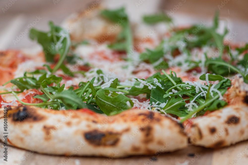 Hot pizza ready to eat with tomato sauce, mozzarella, parmesan cheese and fresh rocket leaves on a wooden board, close up