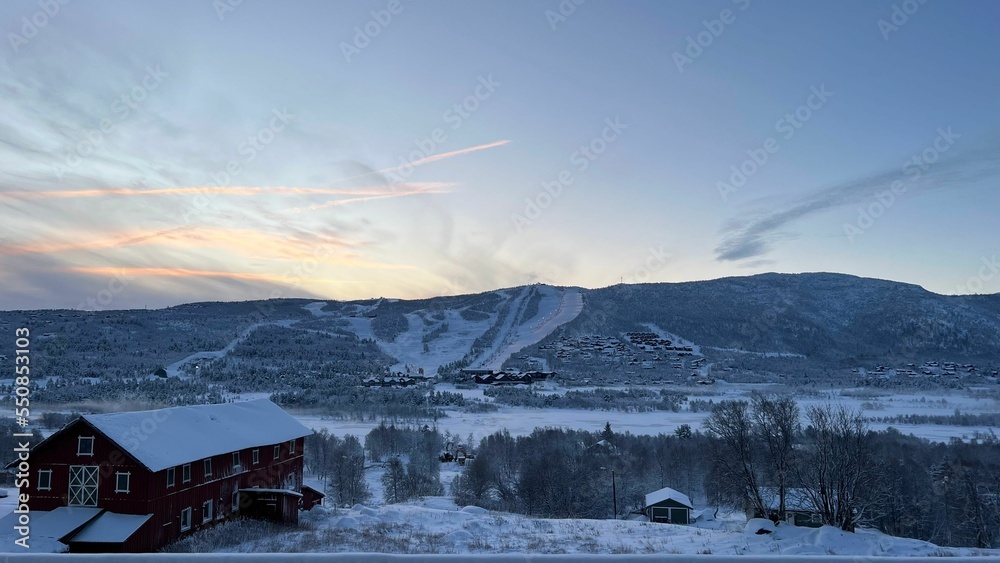 Fototapeta premium Beautiful landscape of a town covered in snow at sunset with a cloudy sky in the background, Norway