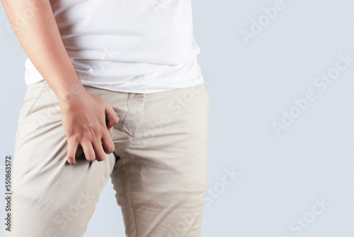 Asian man in reaction of scratching crotch on grey background, closeup. Annoying itch or Tinea Cruris. Human body problem or healthcare and medicine concept. photo