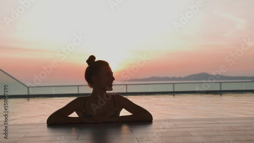 Young and beautiful woman in the rooftop swimming pool at sunset